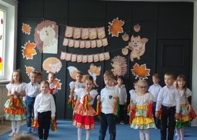 Dzieci w strojach ludowych na scenie z jesiennymi dekoracjami podczas Dnia Edukacji Narodowej.