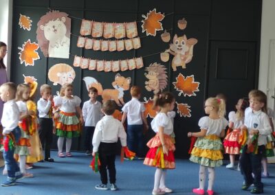 Grupa dzieci w strojach ludowych występuje na tle dekoracji z okazji Dnia Edukacji Narodowej